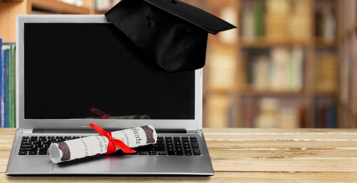Laptop, cappello da universitario e certificato in libreria - Foto di BillionPhotos.com da Adobe Stock
