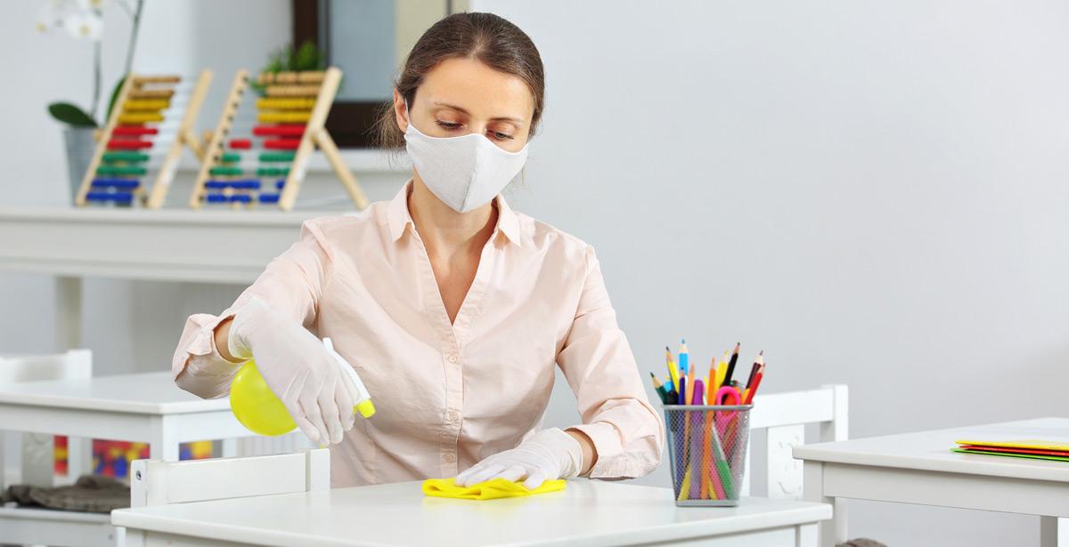 Collaboratrice scolastica pulisce e disinfetta una scrivania - Foto di ShunTerra da Adobe Stock
