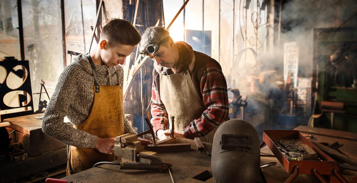Fabbro con apprendista al lavoro in officina - Foto di jackfrog da Adobe Stock