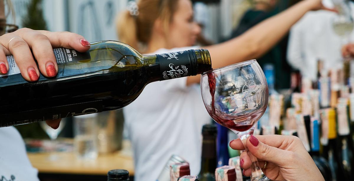 Mano femminile versa vino in un calice ad una fiera - Foto di Евгений Хиль da Adobe Stock