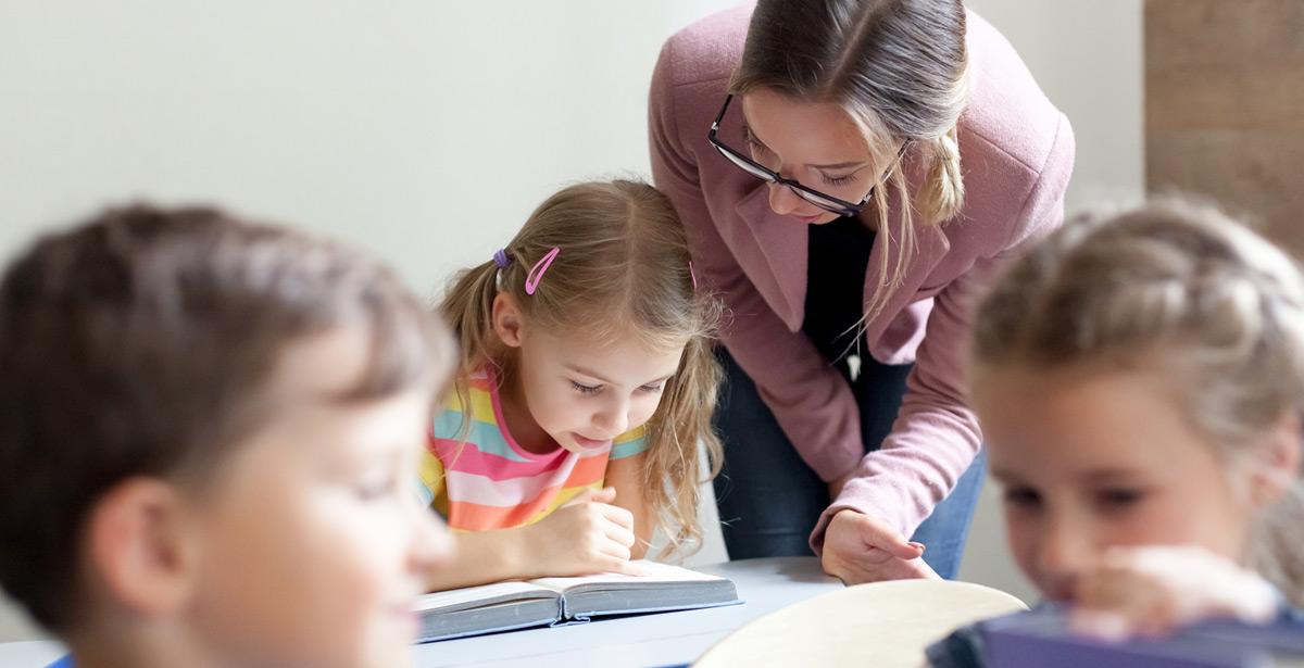 Maestra aiuta una piccola studente in difficoltà - Foto di Marina April da Adobe Stock